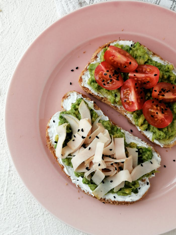 Flat lay of avocado toast with tomatoes and turkey on a pink plate, perfect for a healthy breakfast.